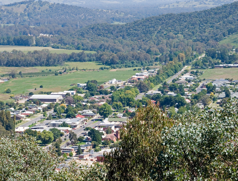 A rural town with a main road, lined with green trees, leading up to hills.