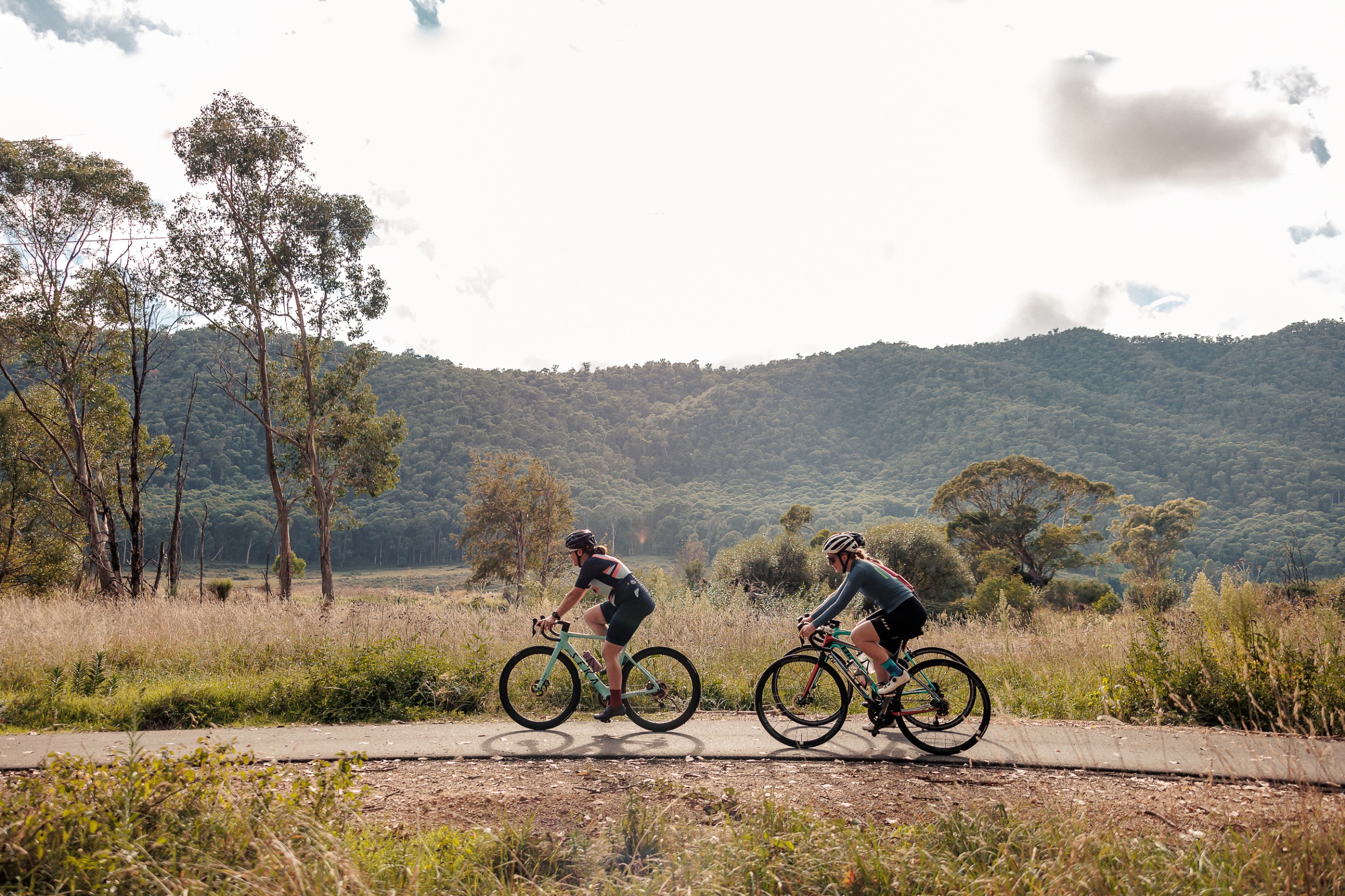 Three cyclists ride along a path with small mountains in the backgrounds.