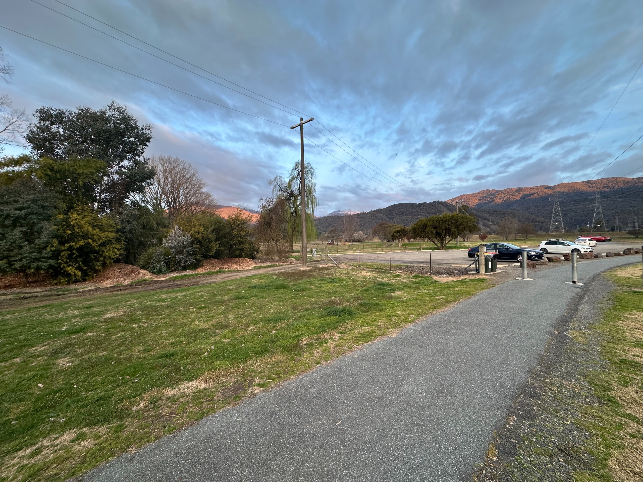 A footpath with lawn on either side, leading up to a car park.